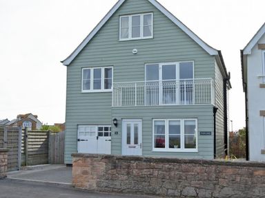 A two-story house with gray siding a white door and windows and a small balcony at Portland in Beadnell