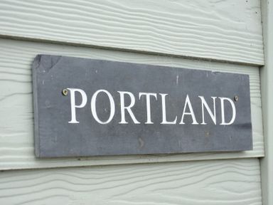 A gray rectangular sign with the word PORTLAND on a light gray wooden wall