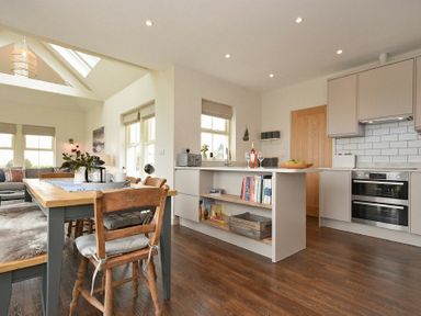 A kitchen and dining area with wooden chairs and table and kitchen island with books at South View nr Bamburgh in Seahouses