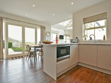 A kitchen with cabinets microwave toaster and a dining table with chairs near glass doors at South View nr Bamburgh in Seahouses