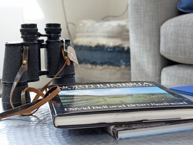 A close-up of binoculars and a book titled Northumbria Collection on a table next to a couch at South View nr Bamburgh in Seahouses