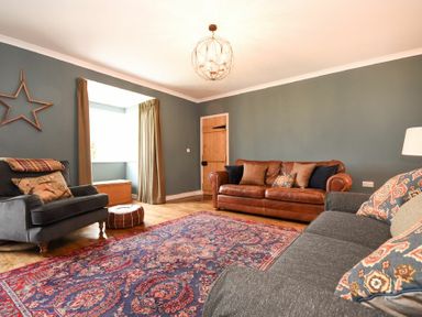 A living room with two sofas a chair a patterned rug and a window with curtains at South View nr Bamburgh in Seahouses