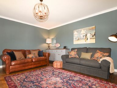 A living room with leather and fabric sofas a patterned rug and a sideboard with a lamp at South View nr Bamburgh in Seahouses