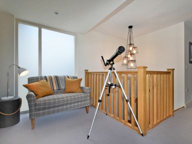 A sitting area with a telescope on a tripod near a wooden staircase railing at South View nr Bamburgh in Seahouses