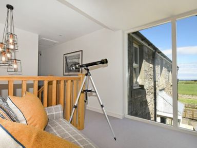 An indoor space with a telescope near a large window and a sofa with cushions at South View nr Bamburgh in Seahouses