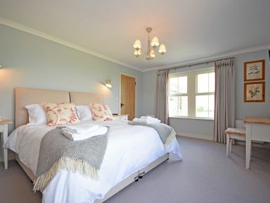 A bedroom with a double bed two bedside tables a window with curtains and a desk at South View nr Bamburgh in Seahouses