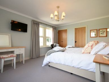 A bedroom with a bed a dressing table a wall mounted TV and two wooden doors at South View nr Bamburgh in Seahouses