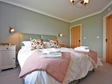 A bedroom with a double bed floral pillows bedside tables and wooden doors at South View nr Bamburgh in Seahouses