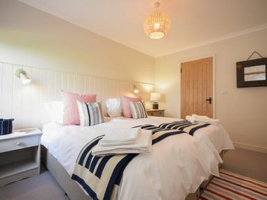 A bedroom with two beds with striped blankets and pillows a door and bedside tables with lamps at South View nr Bamburgh in Seahouses