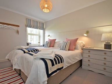 A bedroom with two single beds striped throws and pillows a dresser and a window at South View nr Bamburgh in Seahouses