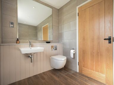 A bathroom with a wall-mounted sink toilet a large mirror and a wooden door at South View nr Bamburgh in Seahouses