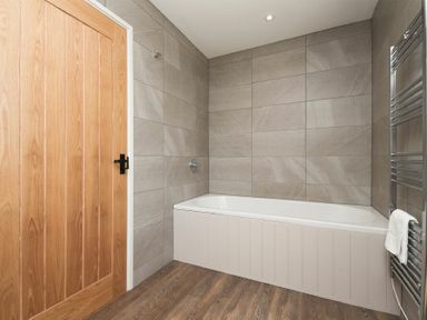 A bathroom with a bathtub wooden door tiled walls and a towel rail at South View nr Bamburgh in Seahouses