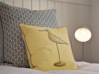 A bed with a yellow pillow featuring a bird design and a patterned pillow behind it at South View nr Bamburgh in Seahouses