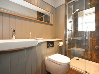 A bathroom with a wall-mounted sink toilet glass shower enclosure and a large mirror at South View nr Bamburgh in Seahouses