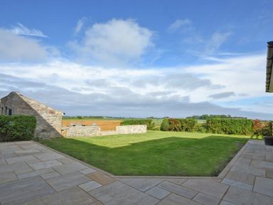 An outdoor area with a tiled patio surrounding a grass lawn and stone walls at South View nr Bamburgh in Seahouses