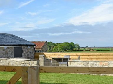 An outdoor patio area with a stone wall wooden fence wicker chairs and a table with a bottle on it at South View nr Bamburgh in Seahouses