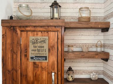 Wooden cabinet with a wifi password sign and wooden shelves with lanterns and glass jars in a room with striped walls at Rivershield in Warkworth