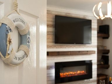 A decorative welcome on board ring hanging on a door with a TV and fireplace in the background at Rivershield in Warkworth
