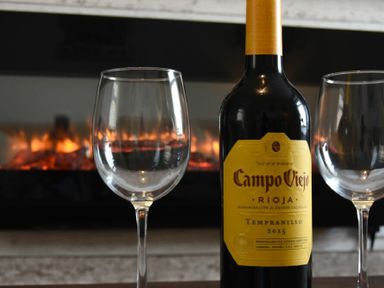A bottle of Campo Viejo Rioja Tempranillo 2015 wine with two empty wine glasses in front of a fireplace at Rivershield in Warkworth