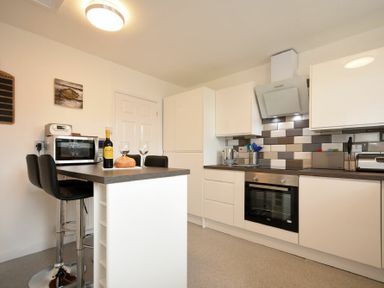 A kitchen with white cabinets a tiled backsplash and two black bar stools by a countertop at Rivershield in Warkworth