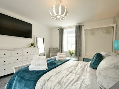 A bedroom with a dresser a wall-mounted TV a window with curtains a bed with pillows and folded towels at Rivershield in Warkworth