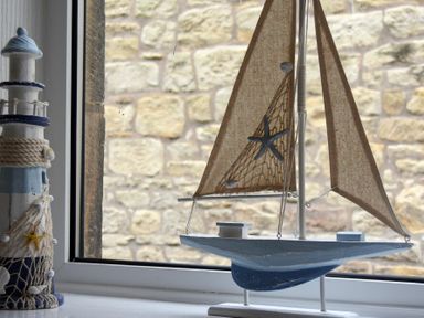 A model sailboat and a decorative lighthouse on a window sill with a stone wall outside at Rivershield in Warkworth