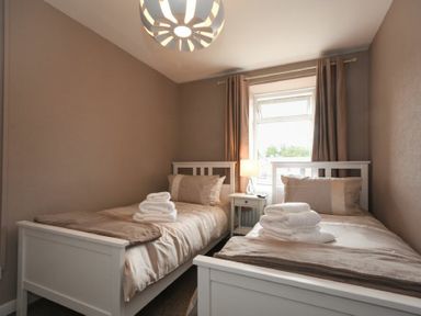A bedroom with two single beds with folded towels on them and a small nightstand with a lamp in between at Rivershield in Warkworth