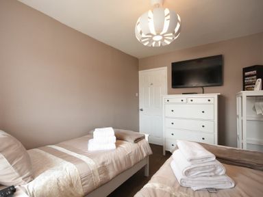 A bedroom with two single beds with folded towels a white dresser a wall-mounted TV and a door at Rivershield in Warkworth