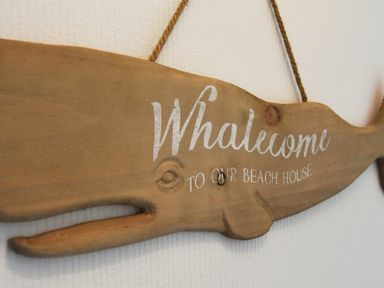 A wooden whale shaped wall decoration with the text Whaleccome to our beach house at Rivershield in Warkworth