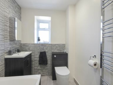 A bathroom with a toilet, sink, cabinet, towel rack, and window at Rivershield in Warkworth