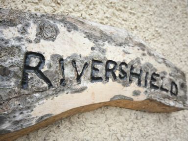 A wooden sign with the word Rivershield carved into it mounted on a textured wall at Rivershield in Warkworth