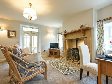 A living room with wicker chairs, a fireplace, a rug, a TV on a wooden stand, and a dining chair at The Lodge Elsdon