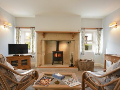 A living room with a stone fireplace and wood stove two armchairs and a wooden table with magazines at The Lodge Elsdon