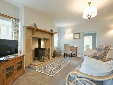 A living room with a TV on a wooden cabinet a fireplace a small desk with a chair and two armchairs at The Lodge (Elsdon) in Elsdon
