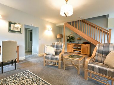 A living room with two plaid armchairs a glass coffee table wooden staircase and a sideboard at The Lodge Elsdon