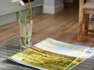 A magazine and a glass vase with a flower on a table at The Lodge (Elsdon) in Elsdon