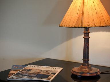 A table lamp with an orange shade next to two magazines on a dark table at The Lodge (Elsdon) in Elsdon