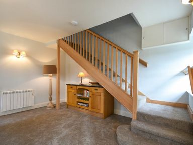 A carpeted staircase with wooden railing with a wooden cabinet and lamps underneath at The Lodge (Elsdon) in Elsdon