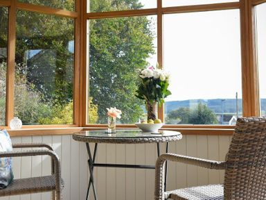 A sunroom with wicker chairs and a round glass table with flowers and fruit on it at The Lodge (Elsdon) in Elsdon