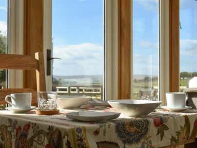 A dining table with cups bowls plates and glasses by a window with a view at The Lodge (Elsdon) in Elsdon