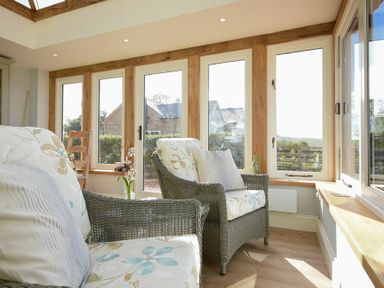A sunroom with wicker armchairs and floral cushions next to large windows at The Lodge Elsdon
