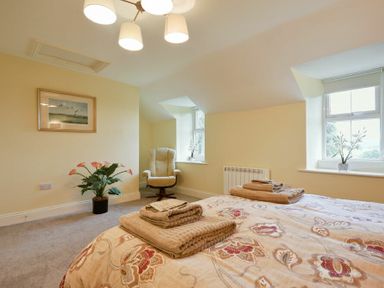 A bedroom with two windows a light brown armchair a plant a framed picture on the wall and folded towels on beds at The Lodge Elsdon