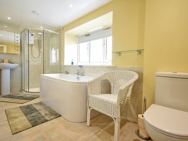 A bathroom with a bathtub shower toilet wicker chair and rugs at The Lodge Elsdon