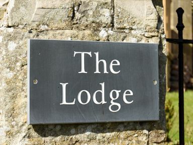 A black sign with the words The Lodge mounted on a stone wall at The Lodge Elsdon