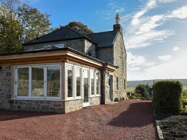 A stone house with a wooden and glass extension in a rural setting at The Lodge (Elsdon) in Elsdon