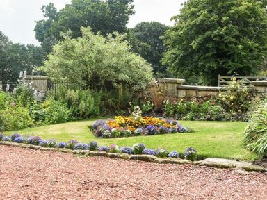 A garden with flower beds green grass a gravel path and stone wall at The Lodge (Elsdon) in Elsdon