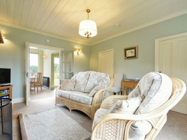 A living room with wicker chairs and a sofa a wooden side table and a TV at Rose Cottage (Elsdon) in Elsdon
