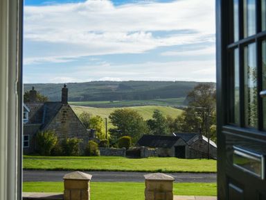 A view of countryside hills and stone houses seen through an open doorway at Rose Cottage Elsdon
