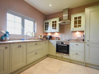 A kitchen with light green cabinets a window above the sink and an oven with a chimney hood at Rose Cottage Elsdon