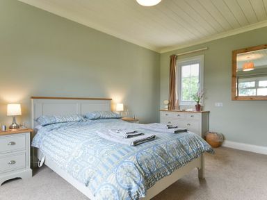 A bedroom with a bed bedside tables lamps a dresser a window and a mirror at Rose Cottage Elsdon